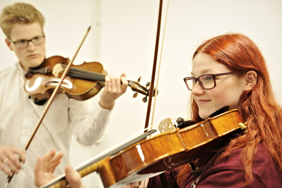 Two violinists performing together, both wearing glasses.